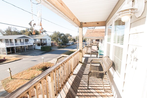 A wooden deck with outdoor furniture, a covered porch, and a view of a street with buildings and cars. - Soundside Oasis: Short Walk to Sound + Linens & Cleaning Included – Sleeps 8 (Kill Devil Hills)