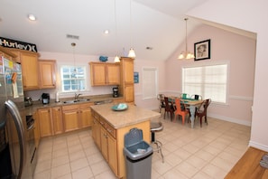 A kitchen with wooden cabinets, a granite countertop, a sink, a trash can, and a dining area with chairs and a table.