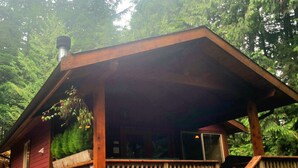 A wooden cabin with a covered porch and a chimney. - Salal Cabin by Evergreen Forest Cabins (Ucluelet)