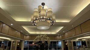 Een ruime lobby met een ronde centrale tafel, een grote kroonluchter en een bloemstuk.