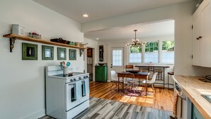 Una cocina con estufa blanca, piso de madera y comedor con mesa y sillas.