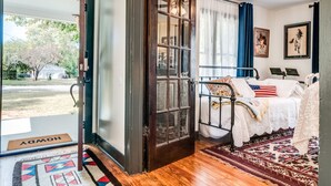 Un dormitorio con cama, ventana con cortinas, puerta y vistas al exterior.
