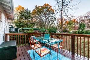 Une terrasse en bois avec une table et des chaises en verre, entourée d’une rambarde.
