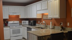 Una cocina con armarios blancos, estufa, microondas, fregadero y encimera de granito.