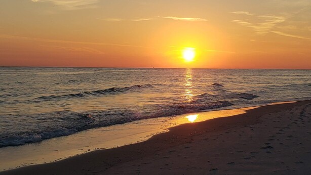 Una playa al atardecer, con el sol reflejándose en el agua.