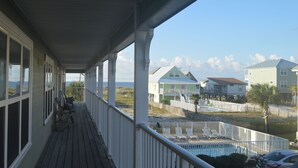 Terraza de madera con zona de piscina, con vistas a una playa con casas y un cielo despejado.