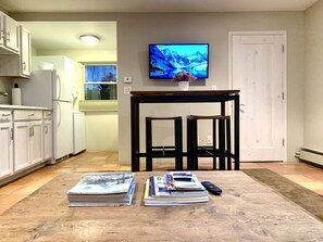 A living room with a wooden coffee table, magazines, a remote control, and a TV displaying a mountain landscape. - Beautiful Casita in downtown. Private Courtyard! (Santa Fe)
