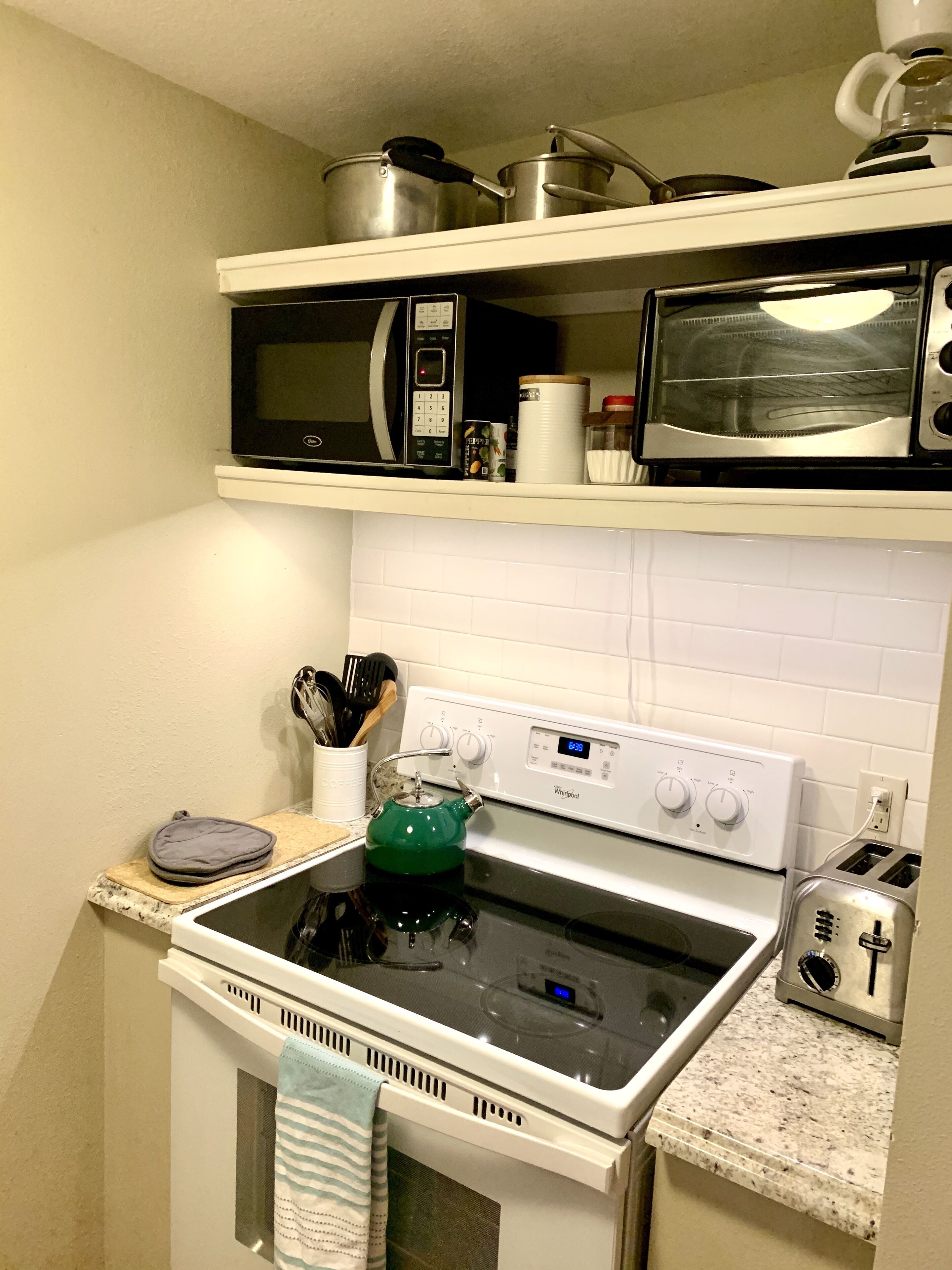 Una cucina con un piano cottura bianco, un forno a microonde e un tostapane. Ci sono pentole sullo scaffale del forno a microonde e un bollitore sul piano cottura.