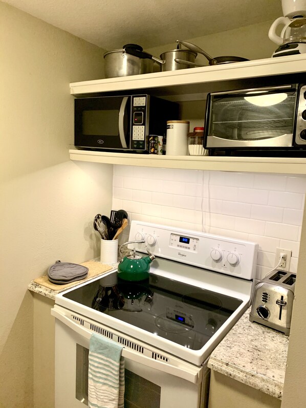 A kitchen with a white stove, a microwave, and a toaster. There are pots on the microwave shelf, and a kettle on the stove.