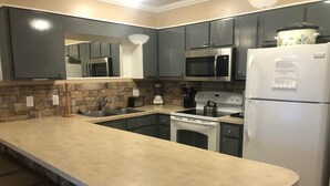 A modern kitchen with grey cabinets, a stainless steel refrigerator, a microwave, an oven, and a sink. - Winterplace Condo E306 (Ghent)