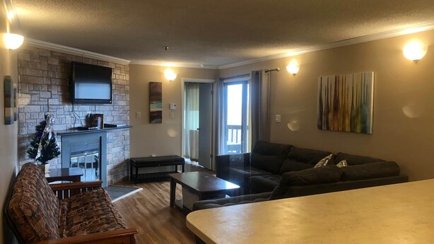 A modern living room with a fireplace, a sofa, a coffee table, and a TV mounted on the wall. - Winterplace Condo E306 (Ghent)