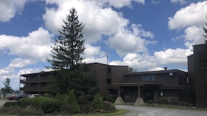 A modern building with a multi-story structure, a parking area, and a large tree in front. - Winterplace Condo E306 (Ghent)