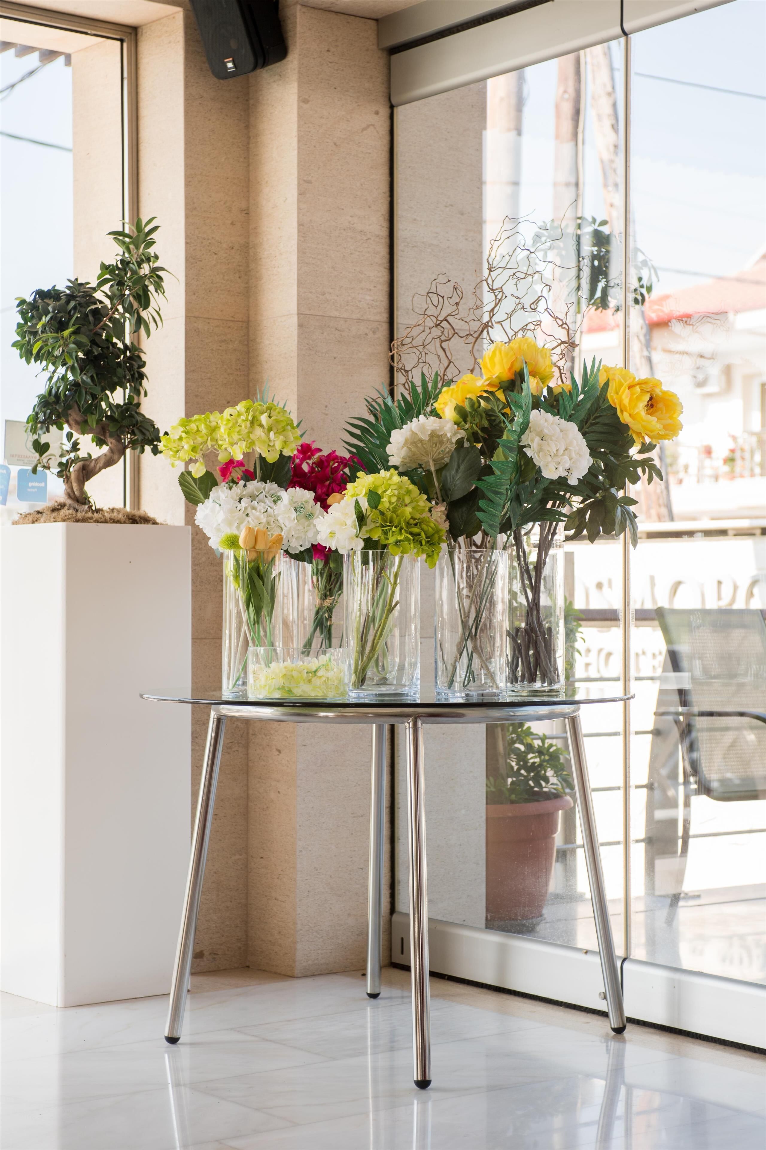 Una mesa de cristal con jarrones de flores y un bonsái.