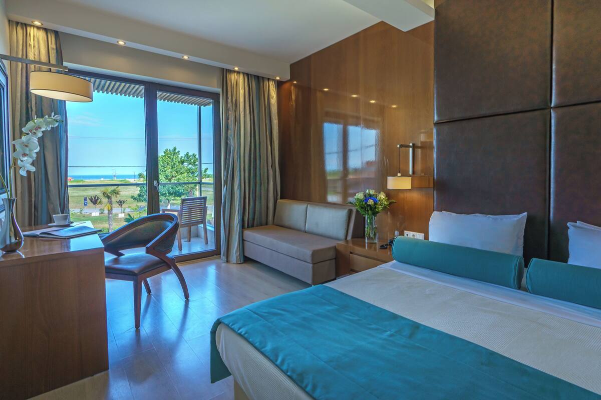 A hotel room with a large bed, a desk, a chair, a sofa, and a view of the outdoors.