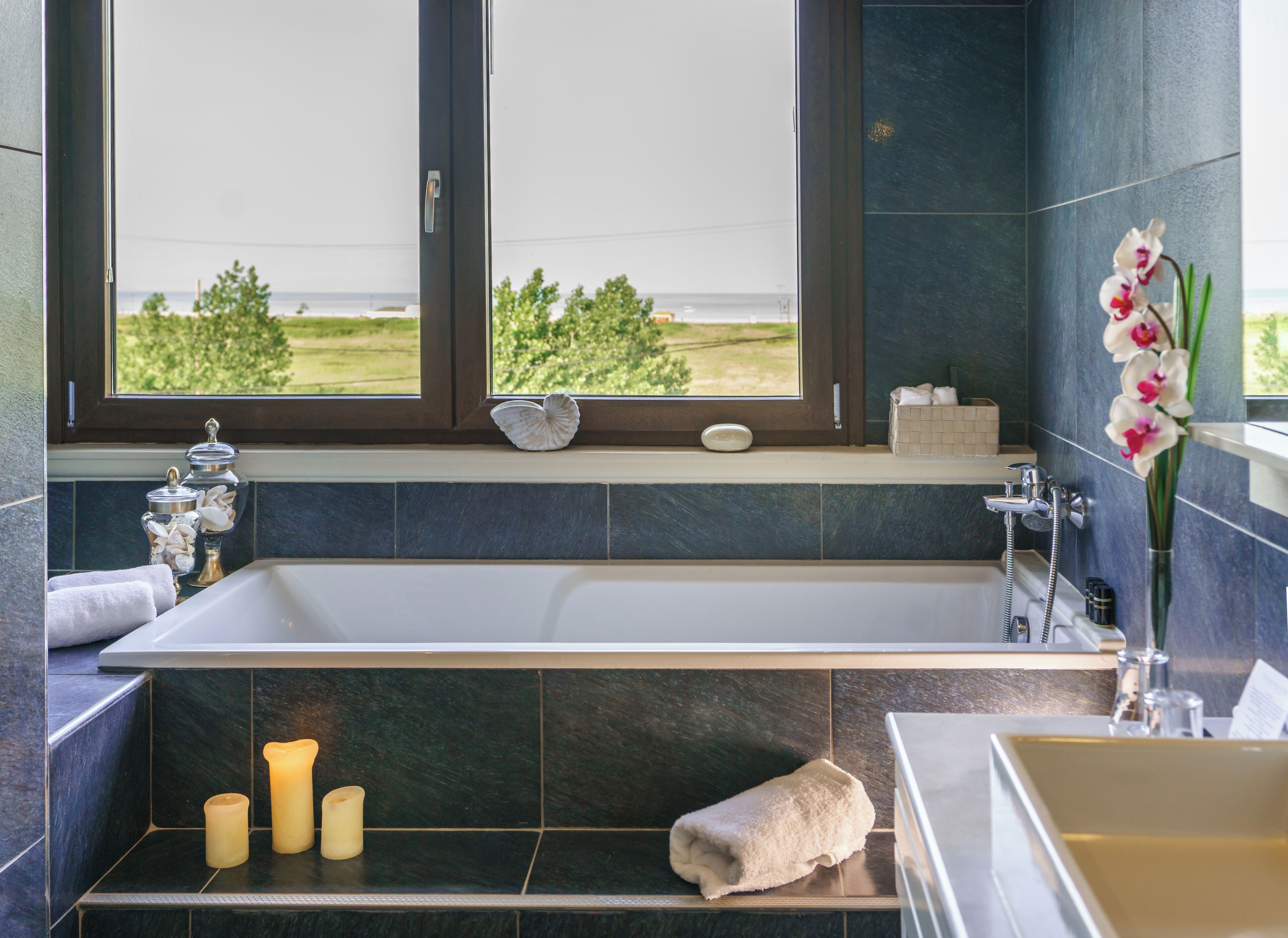A modern bathroom with a bathtub, a shower, and a sink. There are towels, candles, and a vase with flowers on the counter.