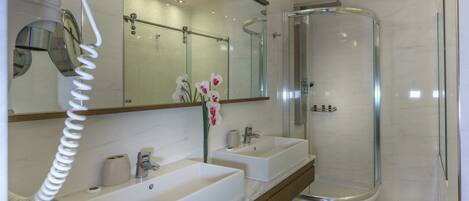 Un baño moderno con dos lavamanos, cabina de ducha de vidrio y un secador de pelo en la pared.