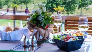 A dining table set with a salad, bread, and a bottle of white wine, with a view of greenery and a wooden bench in the background. - Cosmopolitan Hotel by GHH (Katerini)