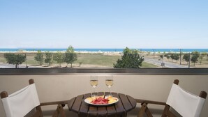A balcony with a table set for two, featuring a plate of fruit and two glasses of white wine, overlooking a beach and ocean. - Cosmopolitan Hotel by GHH (Katerini)
