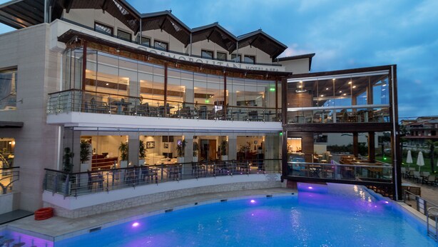 A modern hotel with a large outdoor pool, multiple dining areas, and a well-lit interior. - Cosmopolitan Hotel by GHH (Katerini)