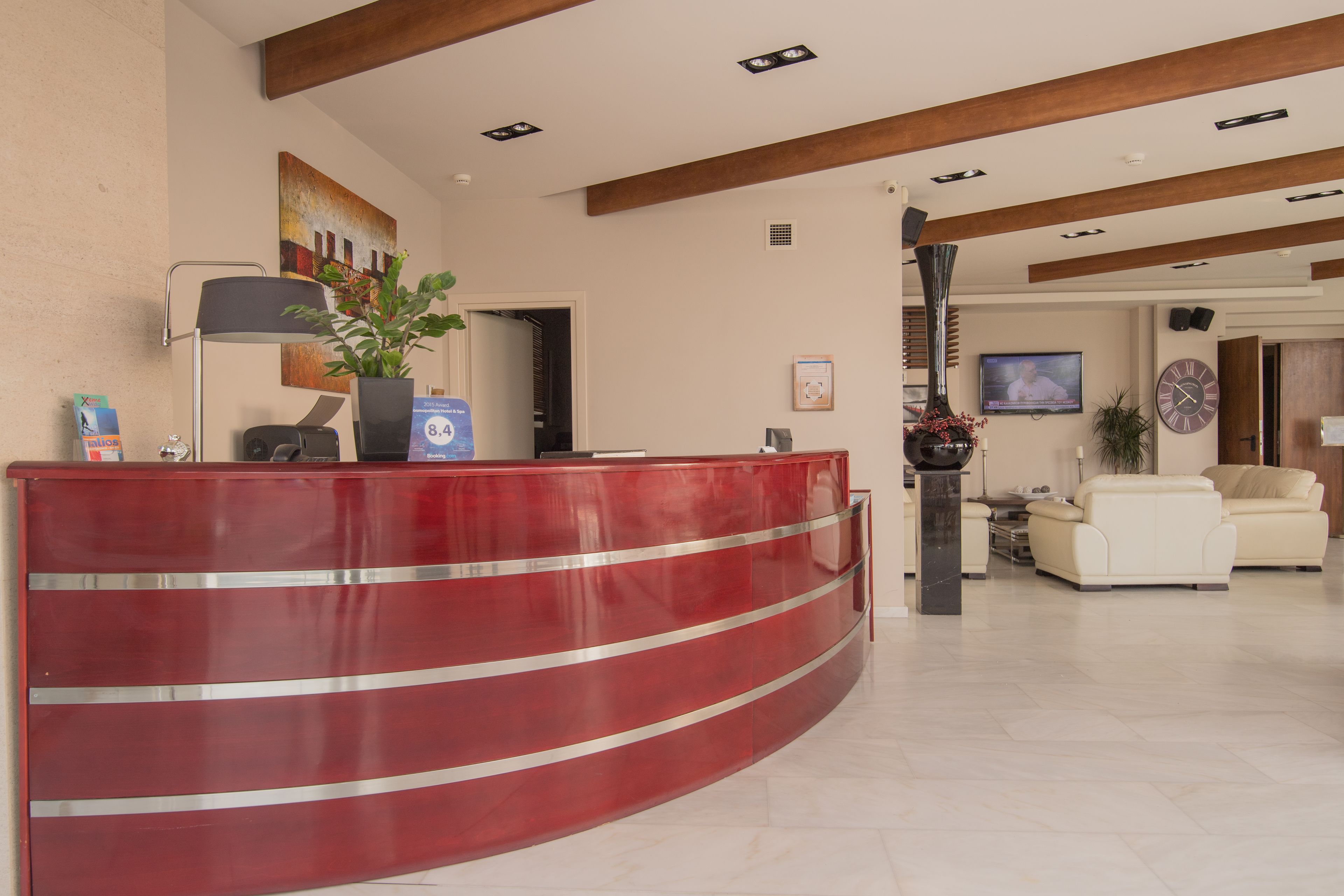 A reception area with a red curved desk, a potted plant, a television, and a clock on the wall.