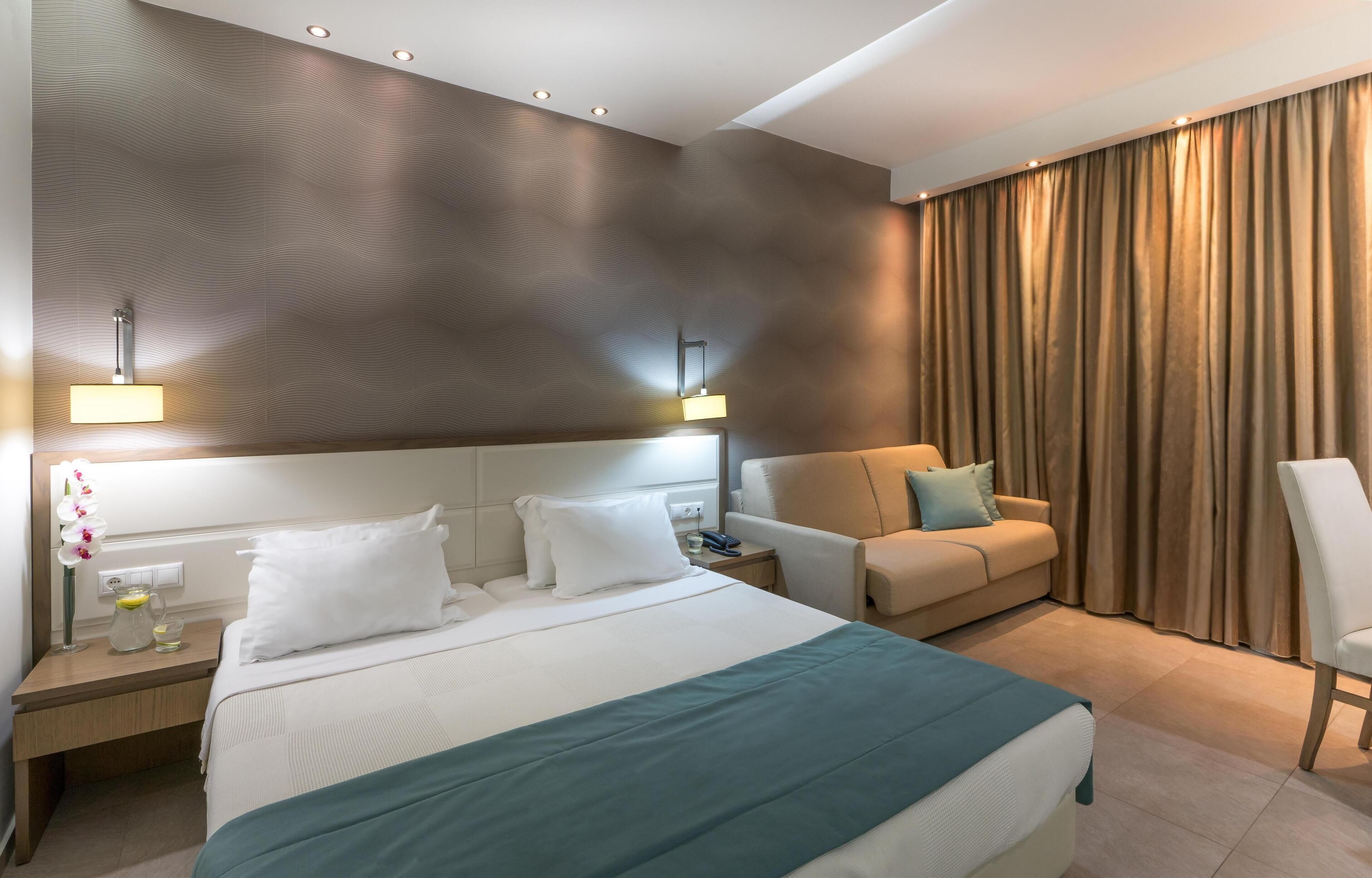 A hotel room with a large bed, a sofa, a desk with a lamp, and a view of the outdoors.