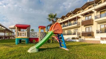 A playground with colorful equipment and a building with balconies in the background.