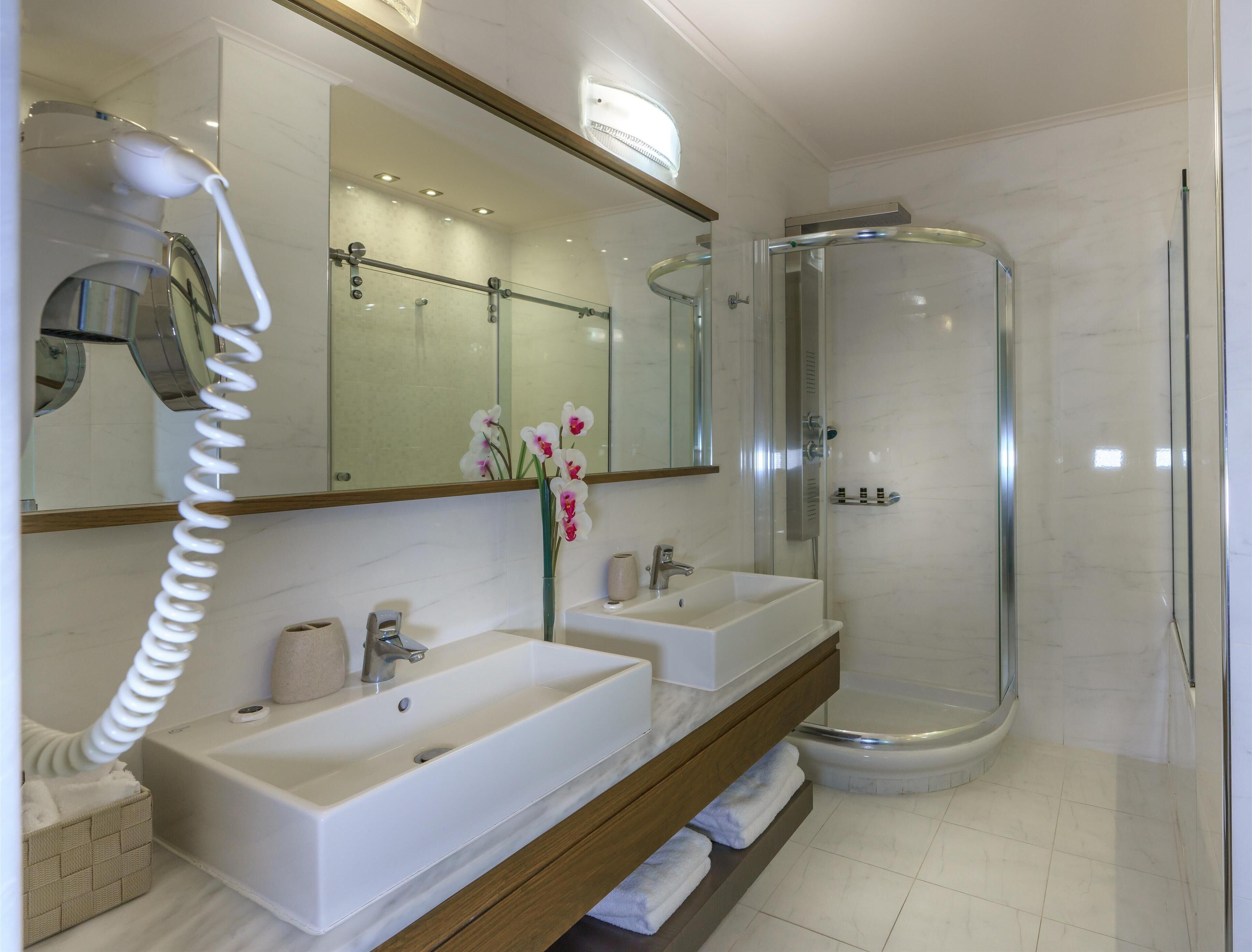 Une salle de bain moderne avec deux lavabos, une douche à parois de verre et un sèche-cheveux posé sur un support.