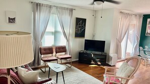 A living room with a sofa, two armchairs, a coffee table, a TV, and a ceiling fan.