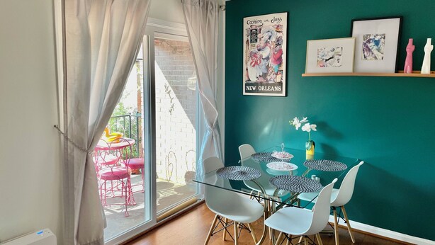 A dining area with a glass table, white chairs, teal walls, and a poster of New Orleans.