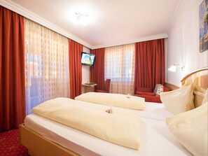 Une chambre d’hôtel avec deux lits, des rideaux rouges, un téléviseur posé sur un meuble et un tableau accroché au mur.