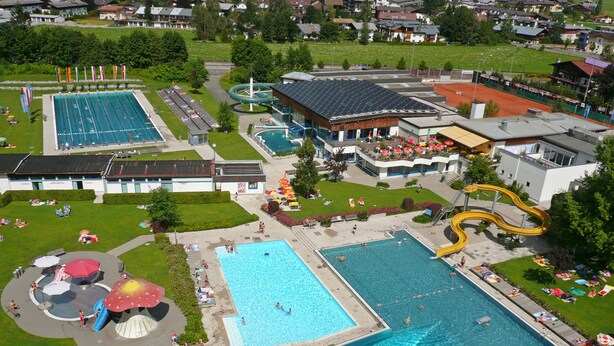 An aerial view of a recreational facility with multiple swimming pools, a water slide, and a covered area with umbrellas. - Familotel St. Johanner Hof (Sankt Johann in Tirol)