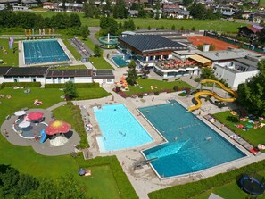 Vue aérienne d’un complexe de loisirs comprenant plusieurs piscines, un toboggan aquatique et un espace abrité avec des parasols.