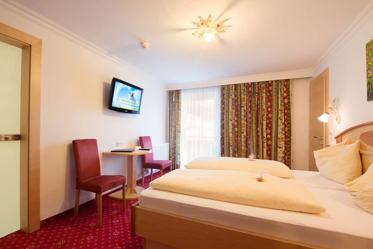 A hotel room with a bed, a desk, a chair, a television, and a window with curtains.