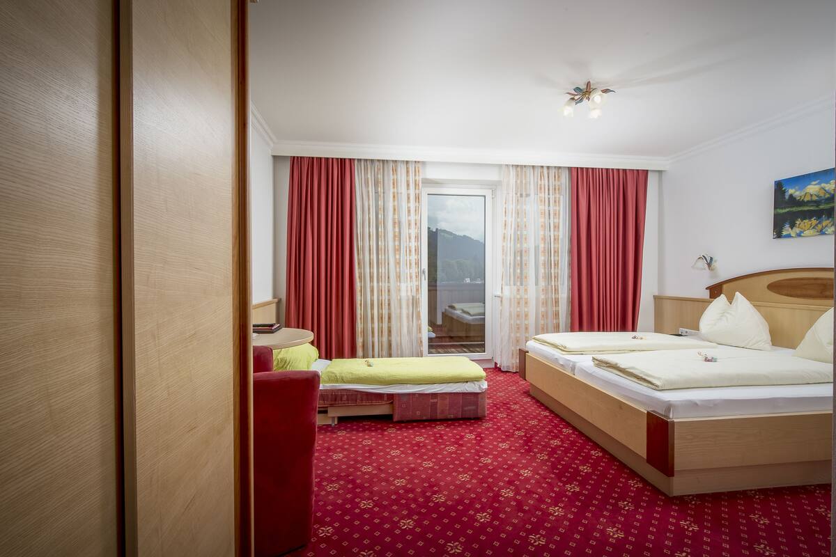 A hotel room with two beds, a red carpet, and a view of a mountainous landscape through the window.