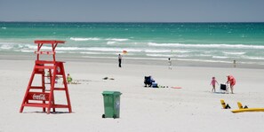 Una playa con una torre de salvavidas, un bote de basura y sillas de playa.