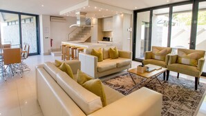 A modern living room with a sofa, armchairs, and a coffee table. There is a kitchen area with a staircase leading to an upper level. - The Gallery Studios (Hermanus)