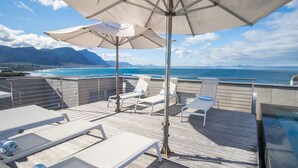 A deck with lounge chairs and umbrellas overlooking a pool and ocean view. - The Gallery Studios (Hermanus)