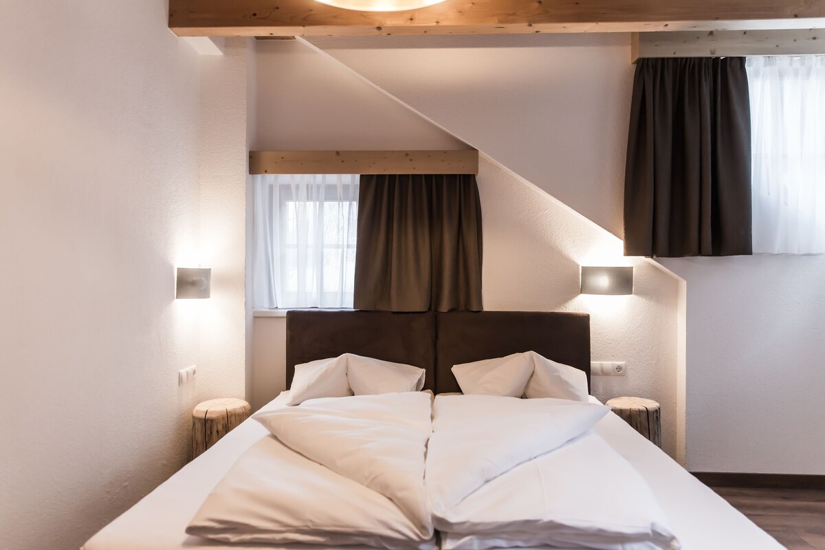 A modern hotel room with a large bed, two bedside tables, and a headboard.