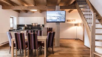 Eine moderne Küche mit weißen Schränken, einem Holzespeisetisch mit gestreiften Stühlen und einem an einem Holzbalken befestigten Fernseher.