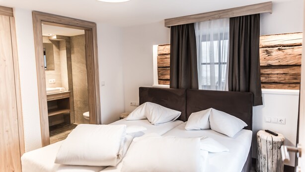A bedroom with a bed, bedside tables, a mirror, and a window with curtains. - A CASA Smaragd (Soelden)