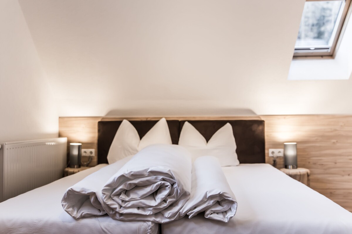 A neatly made bed with white linens and pillows, a wooden headboard, and a skylight above.