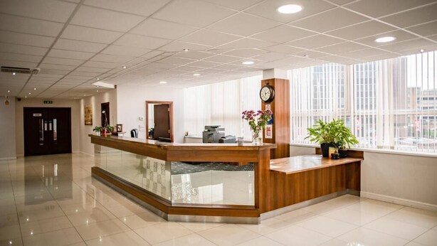 Un moderno mostrador de recepción con una mampara de vidrio, un reloj y plantas en macetas.