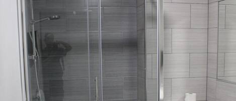 A modern bathroom with a glass-enclosed shower, a toilet, and a towel rack.