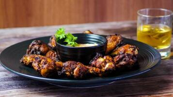 A plate of grilled chicken wings with a dipping sauce and a glass of beer on a wooden table.