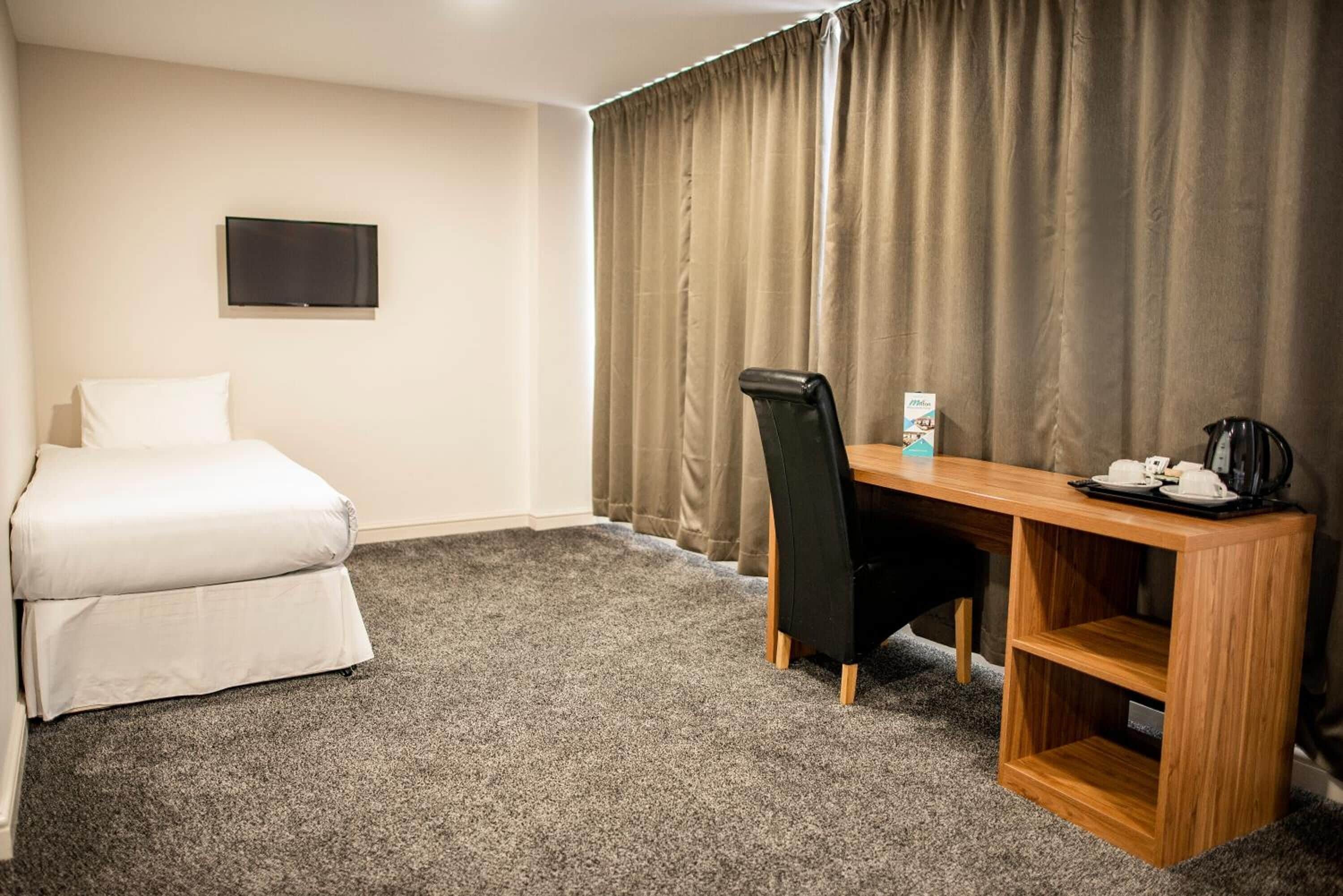 A hotel room with a bed, a desk with a chair, a flat-screen TV, and a coffee maker.