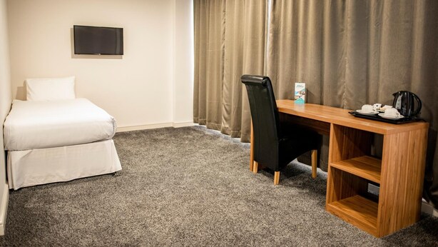 Hotellihuone, jossa on sänky, työpöytä tuolilla, taulutelevisio ja kahvinkeitin.