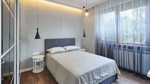 Une chambre à coucher avec un lit, des tables de chevet, une fenêtre avec des rideaux et un luminaire suspendu.