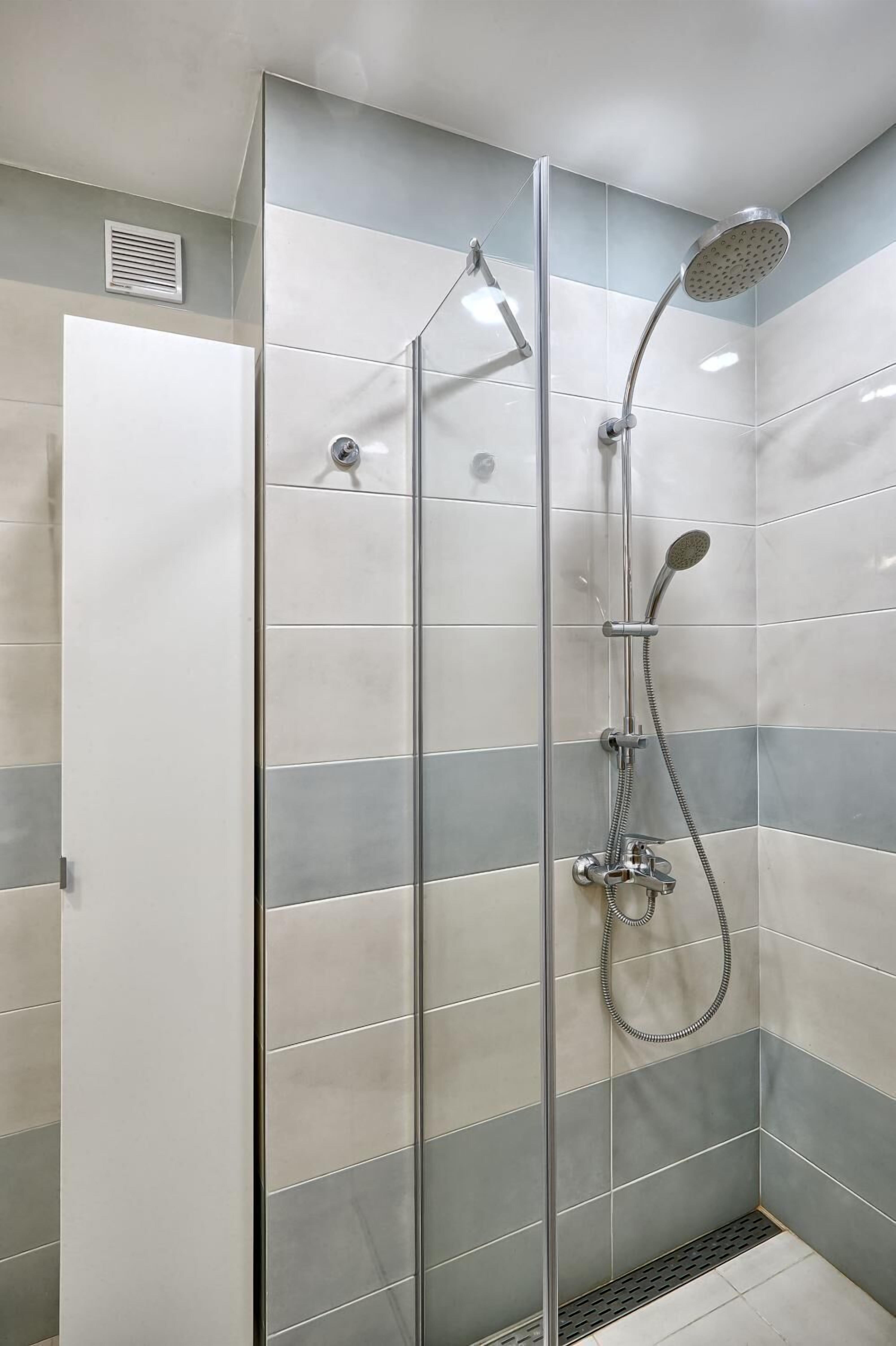 A glass-enclosed shower stall with a handheld showerhead and a wall-mounted rainhead.