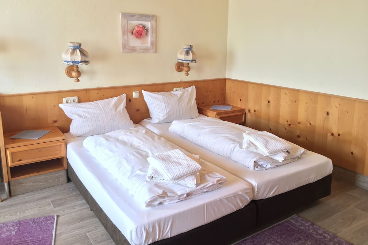 A double bed with white linens and pillows, wooden headboard, bedside tables with lamps, and a framed picture on the wall.