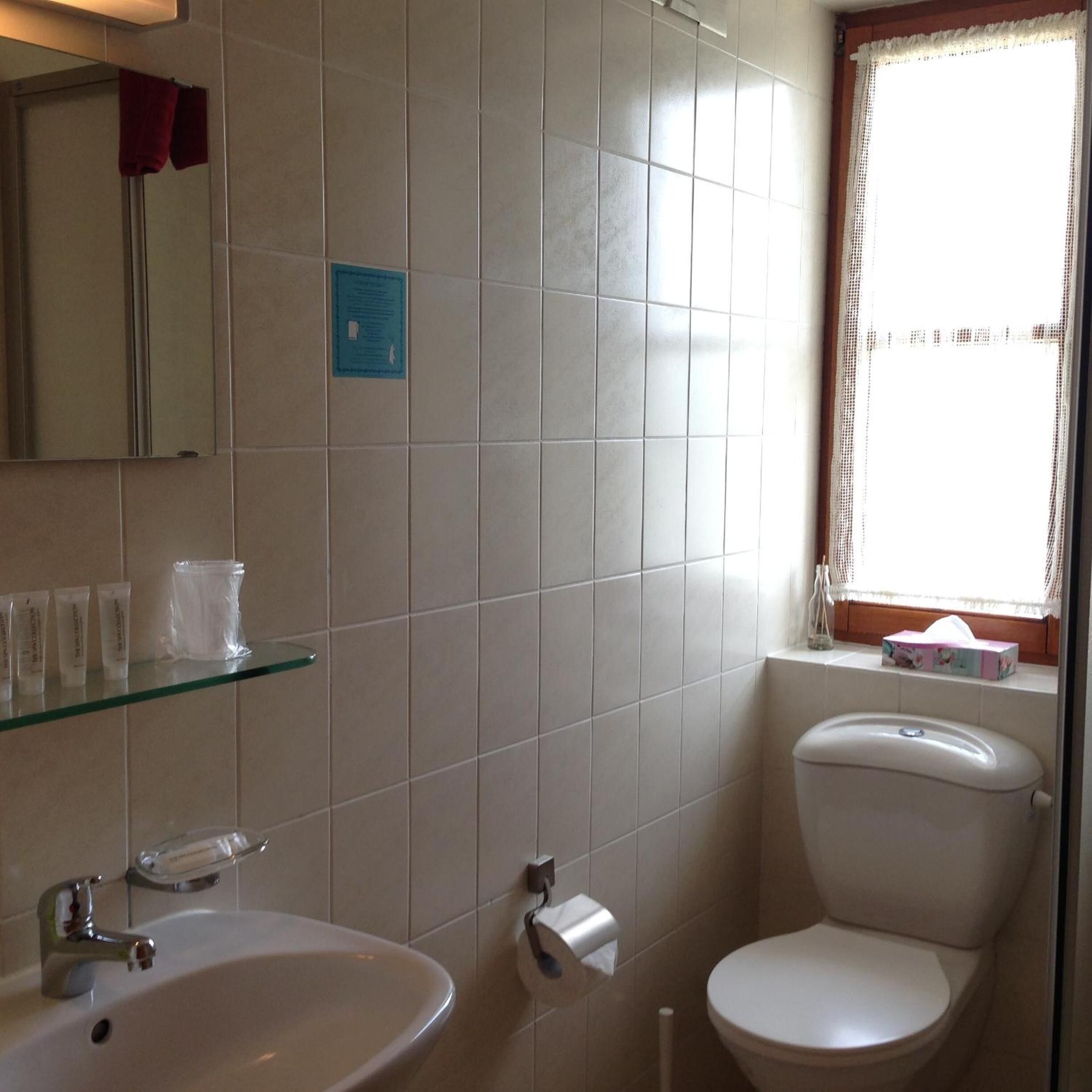 Un baño con inodoro, lavabo y repisa de vidrio con artículos de aseo.